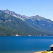 Scenic lake view with mountains and a cozy cabin.